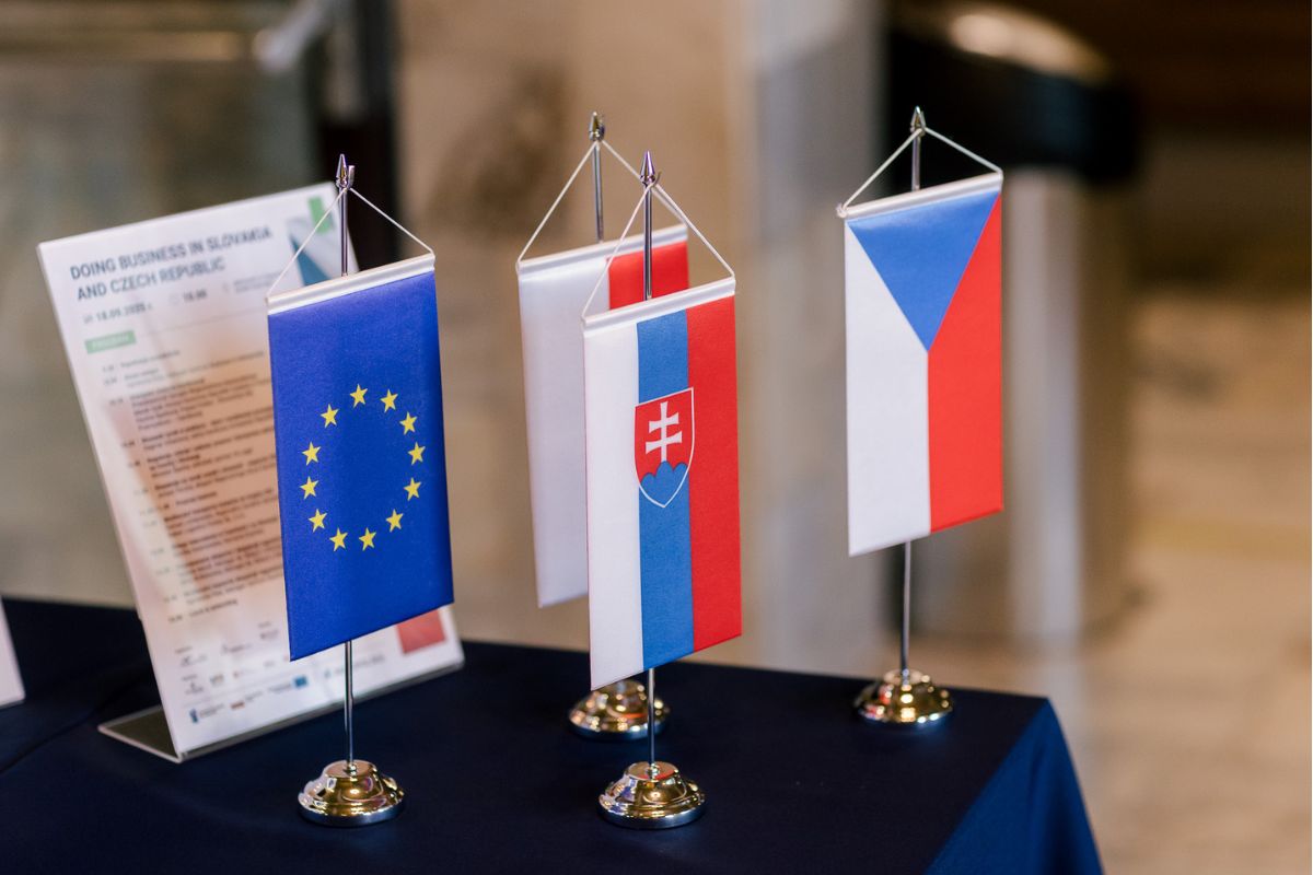 Flagi Unii Europejskiej, Czech, Słowacji i Polski wiszące na małych stojakach pionowo leżące na stole